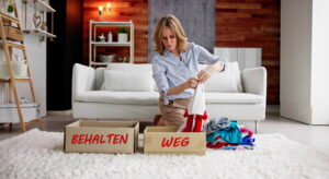 Dame mitleren Alters sitzt im Wohnzimmer hinter zwei Kisten mit Aufschriften 