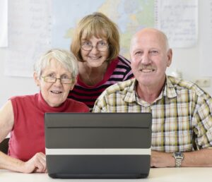 3 ältere Personen hinter einem Laptop, die fröhlich in die Kamera schauen